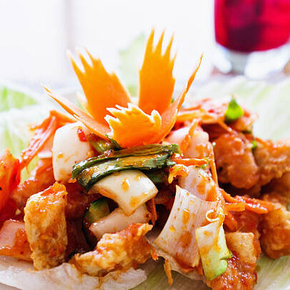 "Thai fish salad: crisply fried fish in batter with chilli, spring onions, tomatoes and sweet and sour sauce, all served in a lettuce cup with the classic Thai carved carrot garnish. A glass of grape juice is in the background."